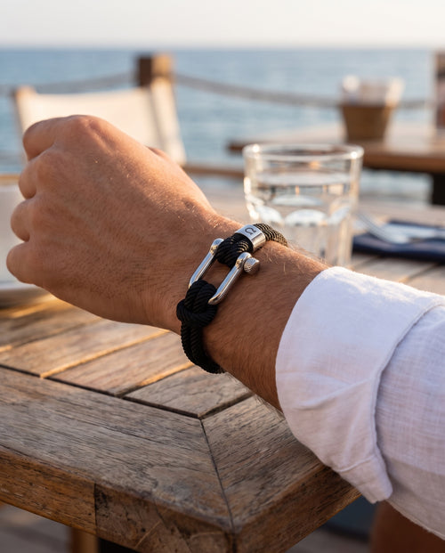 Halyard bracelet on a wrist, forearm on a teak table by the sea