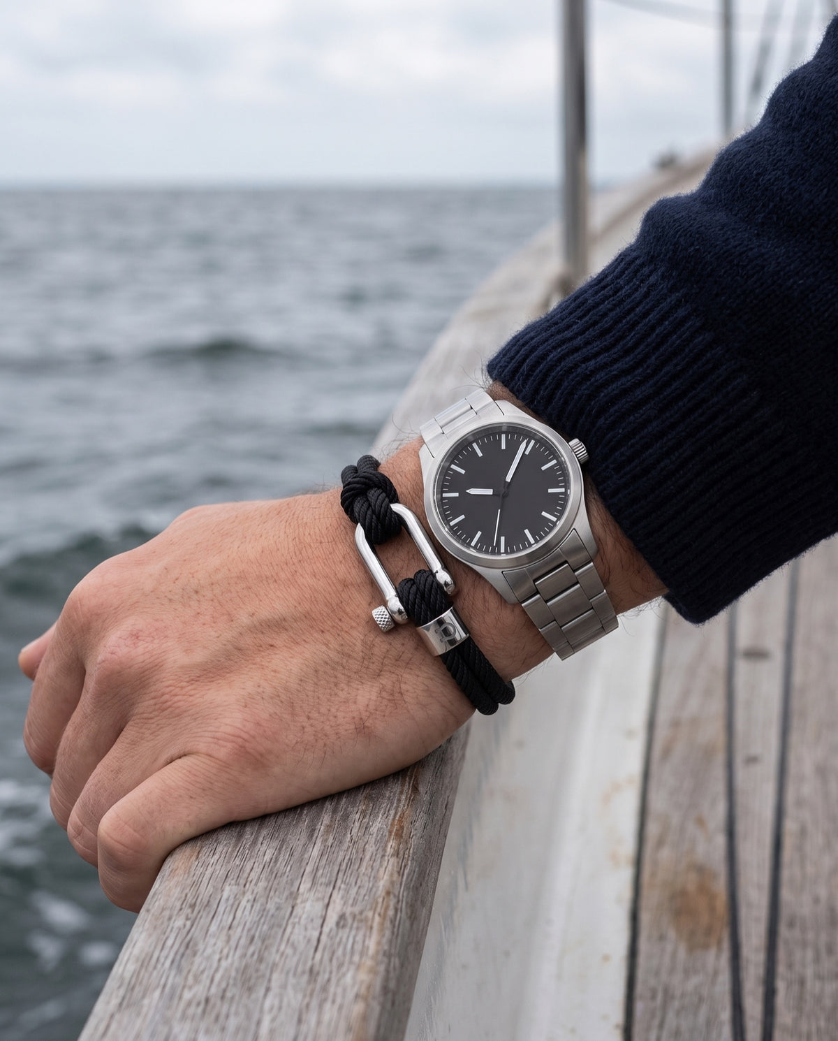 Halyard bracelet worn with a steel watch, hand on a boat rail